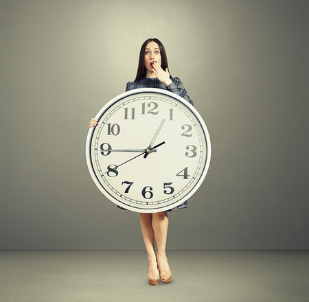 full-length portrait of amazed woman with big white clock over grey backgroundの写真素材
