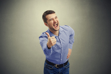 excited man screaming and showing thumbs up over dark backgroundの写真素材