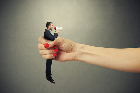 big female hand holding in fist small man and he screaming at megaphone. photo on dark backgroundの写真素材