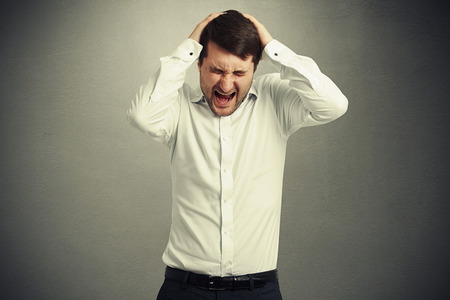 emotional creaming man in white shirt holding his head and closed his eyes strongly over grey backgroundの写真素材