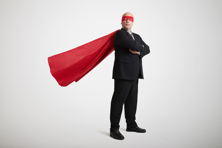 senior businessman dressed as a superhero in red mask and cloak over light grey backgroundの写真素材