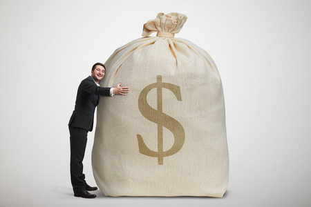 happy man embracing big bag with money over light grey backgroundの写真素材