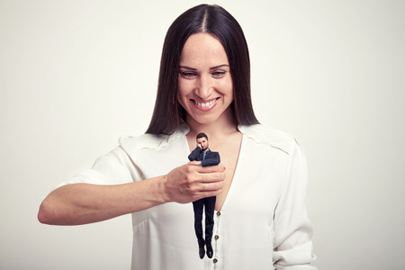 smiley woman holding small wearied man in her fist over light grey backgroundの写真素材
