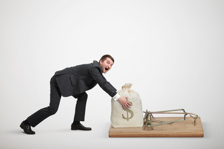 amazed man in formal wear reaching his hands to take bag with money in big mousetrap over light grey backgroundの写真素材
