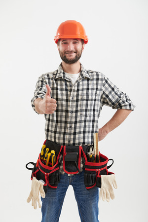 smiley workman with tools in orange helmet showing thumbs up over light backgroundの写真素材