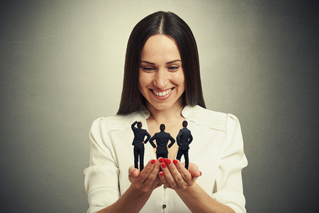 smiley woman holding three men on her palms and looking at them over dark backgroundの写真素材