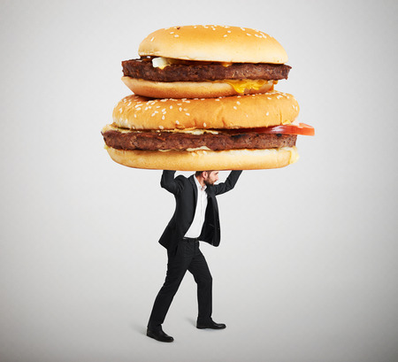 small man in formal wear carrying big sandwiches overhead against light grey backgroundの写真素材