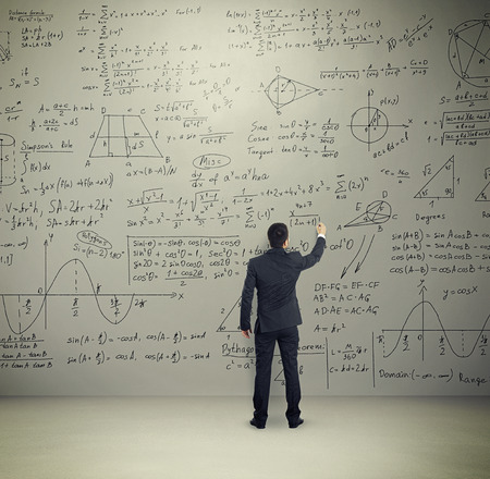 man in formal wear writing formulas on big grey wall