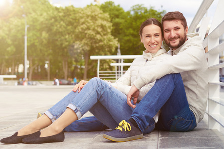 urban photo of smiley young couple sitting and looking at cameraの写真素材