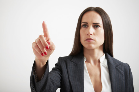 serious businesswoman holding her forefinger like pushing button on virtual screen over light grey backgroundの写真素材