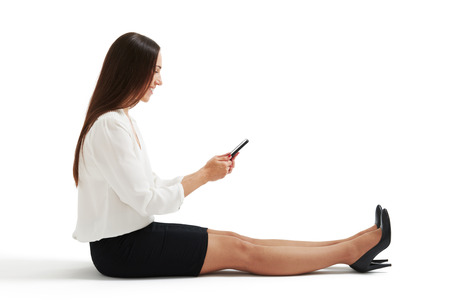 sideview photo of woman in formal wear sitting on the floor and using her smartphone. isolated on white backgroundの写真素材