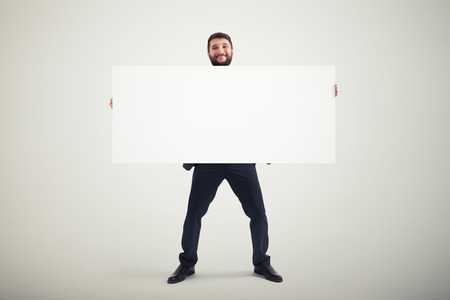 smiley businessman holding empty banner and looking at camera over grey backgroundの写真素材