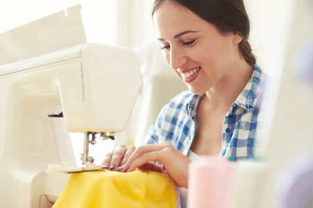 smiley young woman seamstress sewing yellow dressの写真素材