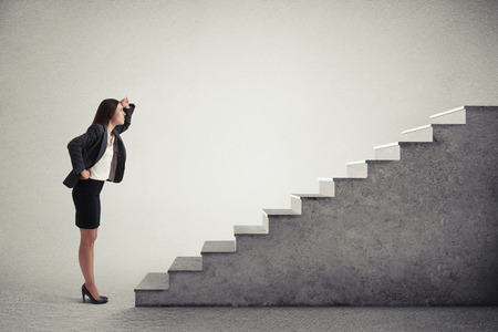 serious woman looking up at top of concrete stairway over light grey backgroundの写真素材