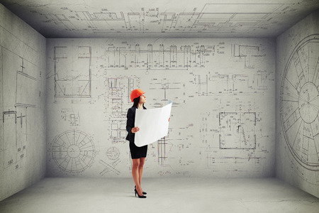 businesswoman in hardhat with blueprint looking up at prints on the walls and ceilingの写真素材