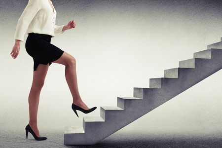 businesswoman in formal wear walking up stairs over light grey backgroundの写真素材