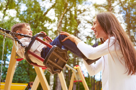 happy mother pushing laughing son on swing in a parkの写真素材