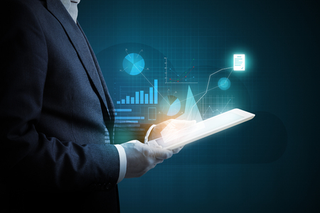 man with tablet pc analyzing virtual diagrams of financial activity over dark backgroundの写真素材