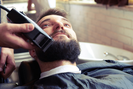 barber shaving beard with electric razor in vintage barber shopの写真素材