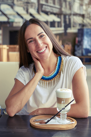 smiley young woman sitting in cafe with cappuccino and looking at cameraの写真素材