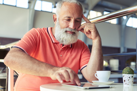 bearded senior man using tablet pc in cafeの写真素材