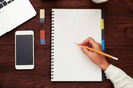 top view of womans hand holding pencil and ready to writing on empty white notepad over wooden tableの写真素材