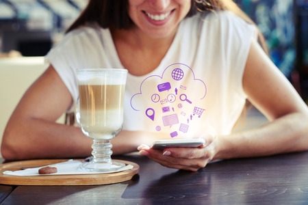 portrait of smiley young woman sitting in cafe and using her smartphone. virtual icons floating in the airの写真素材