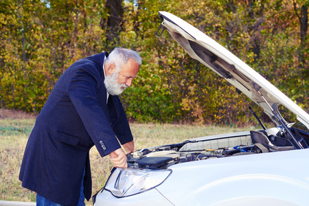 senior man looking under the hood of breakdown car at outdoorの写真素材
