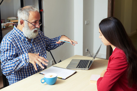 bearded senior man explaining something to young woman in his officeの写真素材