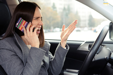 emotional woman driving the car, holding the mobile phone and screamingの写真素材
