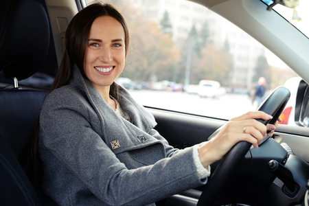 smiley beautiful woman driving a car and looking at cameraの写真素材