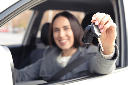 smiley woman sitting in car and showing the car keys. focus on the keys