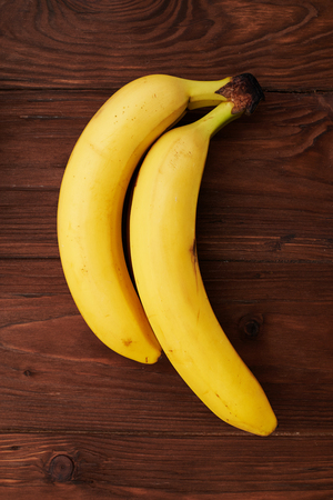 two yellow fresh bananas on brown wooden backgroundの写真素材