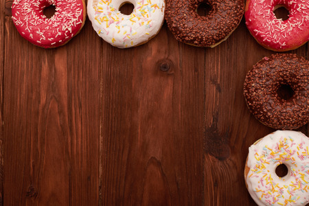 colorful donuts lying on brown wooden table like a frame with empty copyspaceの写真素材