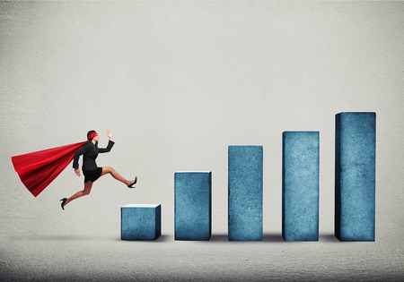 purposeful businesswoman in superhero cloak running up on diagram over grey backgroundの写真素材