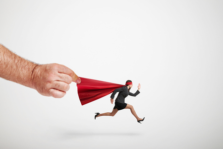 big mans hand holding the red cloak of running superwoman over light grey backgroundの写真素材