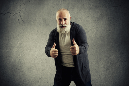 smiley bearded man showing thumbs up and looking at camera over dark backgroundの写真素材