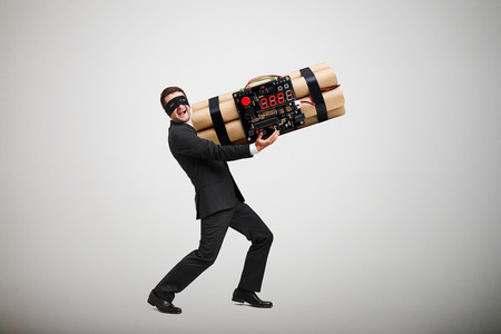 laughing offender in black mask carrying big bomb and looking at camera over light grey backgroundの写真素材