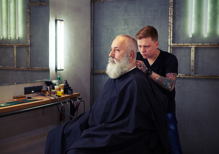 Barber cutting hair to handsome attractive serious man with beard in the barbershopの写真素材