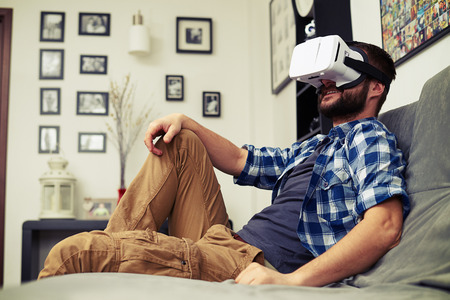 Young Caucasian man resting on comfortable sofa wearing VR headset glassesの写真素材