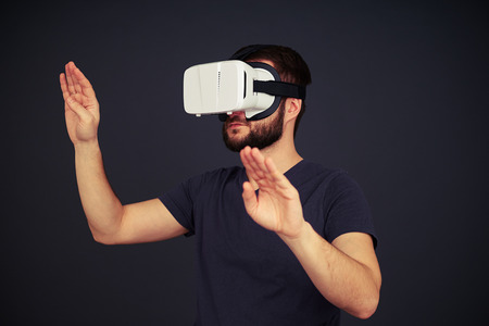 Beard man touch something with both hands and looks to the right side in virtual reality, on black...