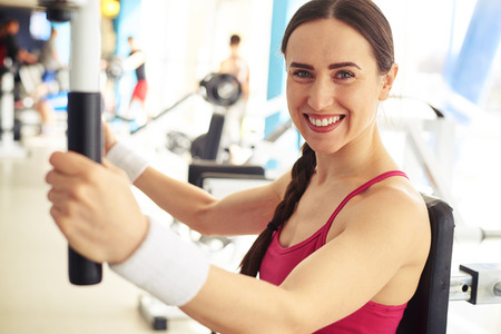 Young beautiful smiling woman is working out on butterfly machine at the gymの写真素材