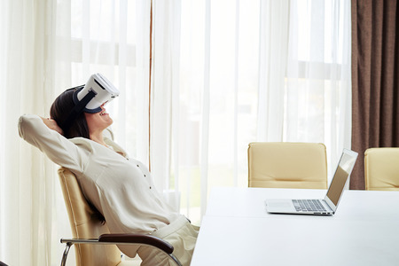 Young pretty woman is smiling and feels relaxed while watching something in virtual reality glassesの写真素材