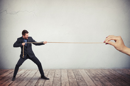A man in dark business suit is vigorously pulling the rope from the one end while a female's hand is holding another end of the ropeの写真素材
