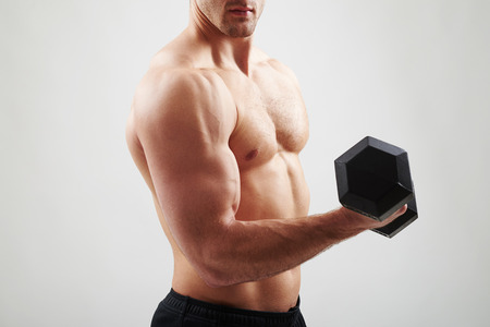 Close-up of bare-chested athletic guy who is holding a dumbbell in his hand and showing muscles on white backgroundの写真素材