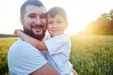 Portrait of happy smiling dad and son in the sunlit field during sunsetの写真素材