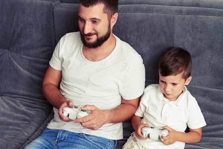 Small boy is willing to win while playing a videogame with his dad using joysticksの写真素材