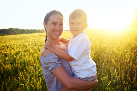 Portrait of young mother and her small son in the field during beautiful sunset