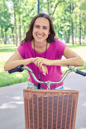 Close-up of smiling beautiful woman who is posing on bicycle with basket in recreational areaの写真素材