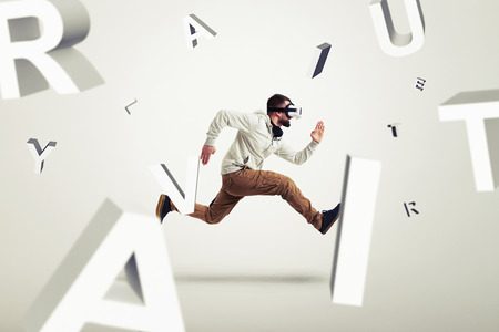 Young man in casual clothes and virtual reality glasses is running between 3d letters over white backgroundの写真素材